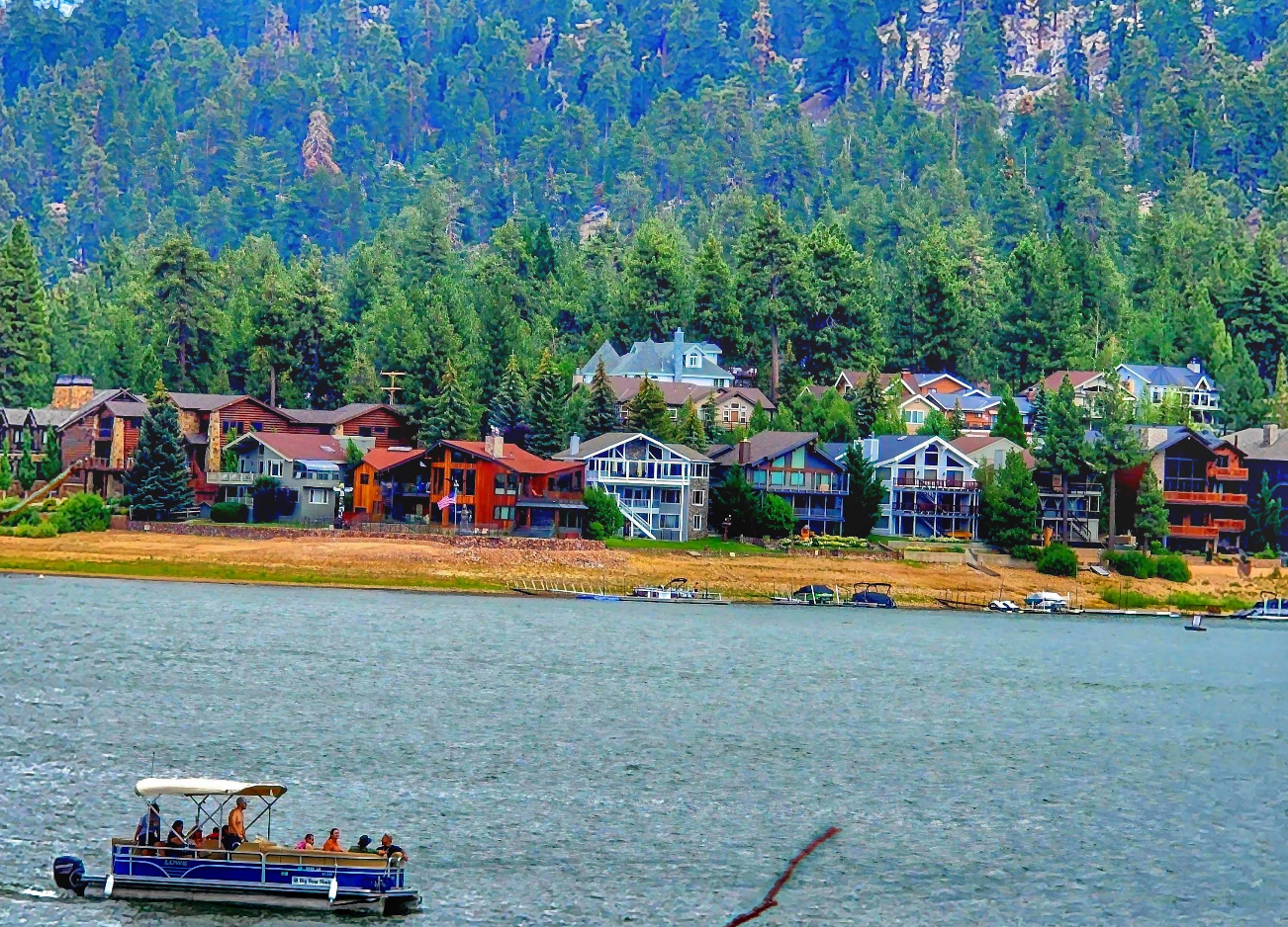 A group of people ride a small boat on a lake in one of the picturesque lake towns, with colorful houses and dense pine trees lining the shore and mountains rising in the background.