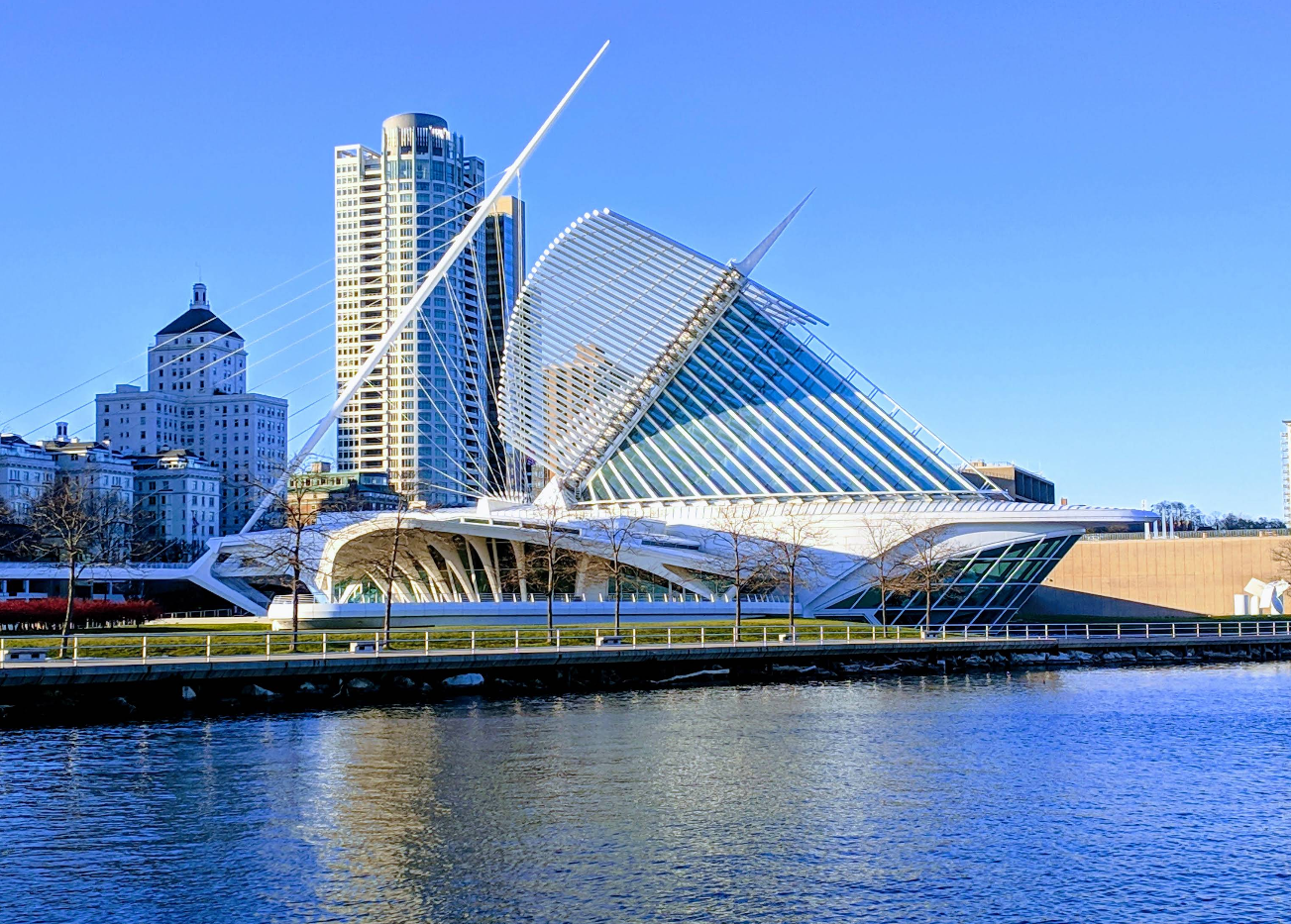 The Milwaukee Art Museum, with its distinctive white, wing-like brise soleil, stands by the waterfront on a clear day. Travelers save photos of its striking silhouette against the tall modern and historic buildings in the background.