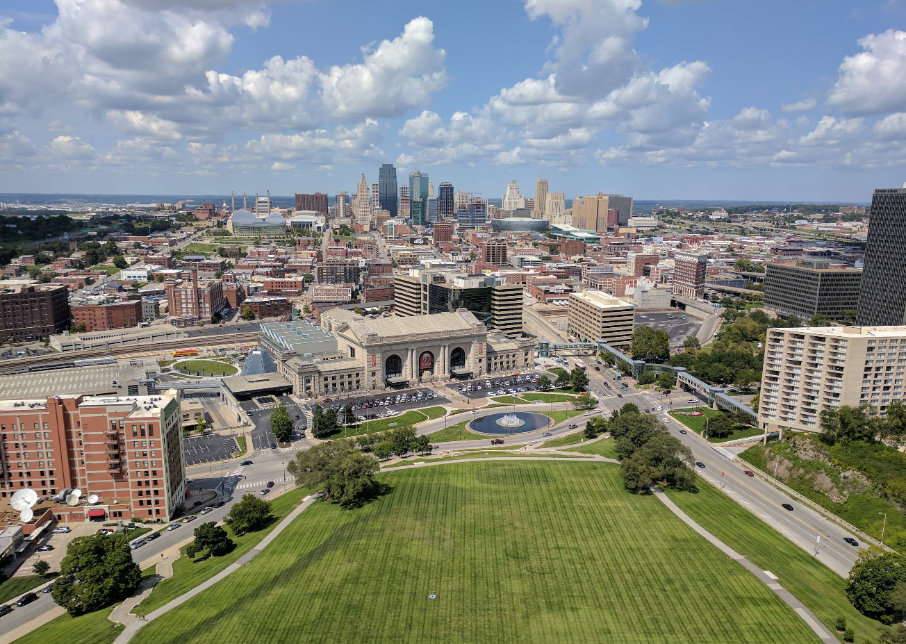 Aerial view of downtown Kansas City, Missouri, featuring Union Station in the center, a circular fountain, green lawn, and skyline—an inviting scene where travelers save while exploring iconic sights under a partly cloudy sky.