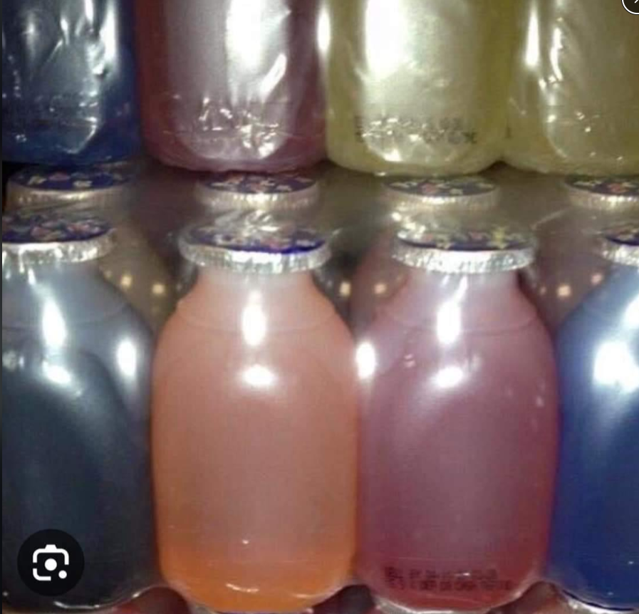Plastic bottles of assorted pastel-colored yogurt drinks are packed closely together in shrink wrap, arranged in two rows. The colors include purple, yellow, pink, and blue, with foil lids sealed on top.