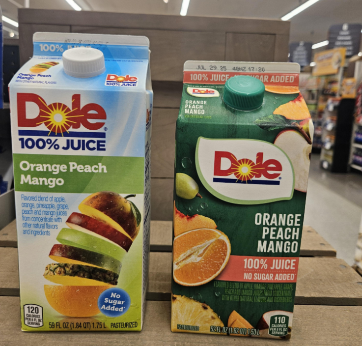 Two cartons of Dole 100% Juice Orange Peach Mango on a store shelf. The left carton is blue and white with images of stacked fruit slices, while the right carton is green with images of whole and sliced fruit.