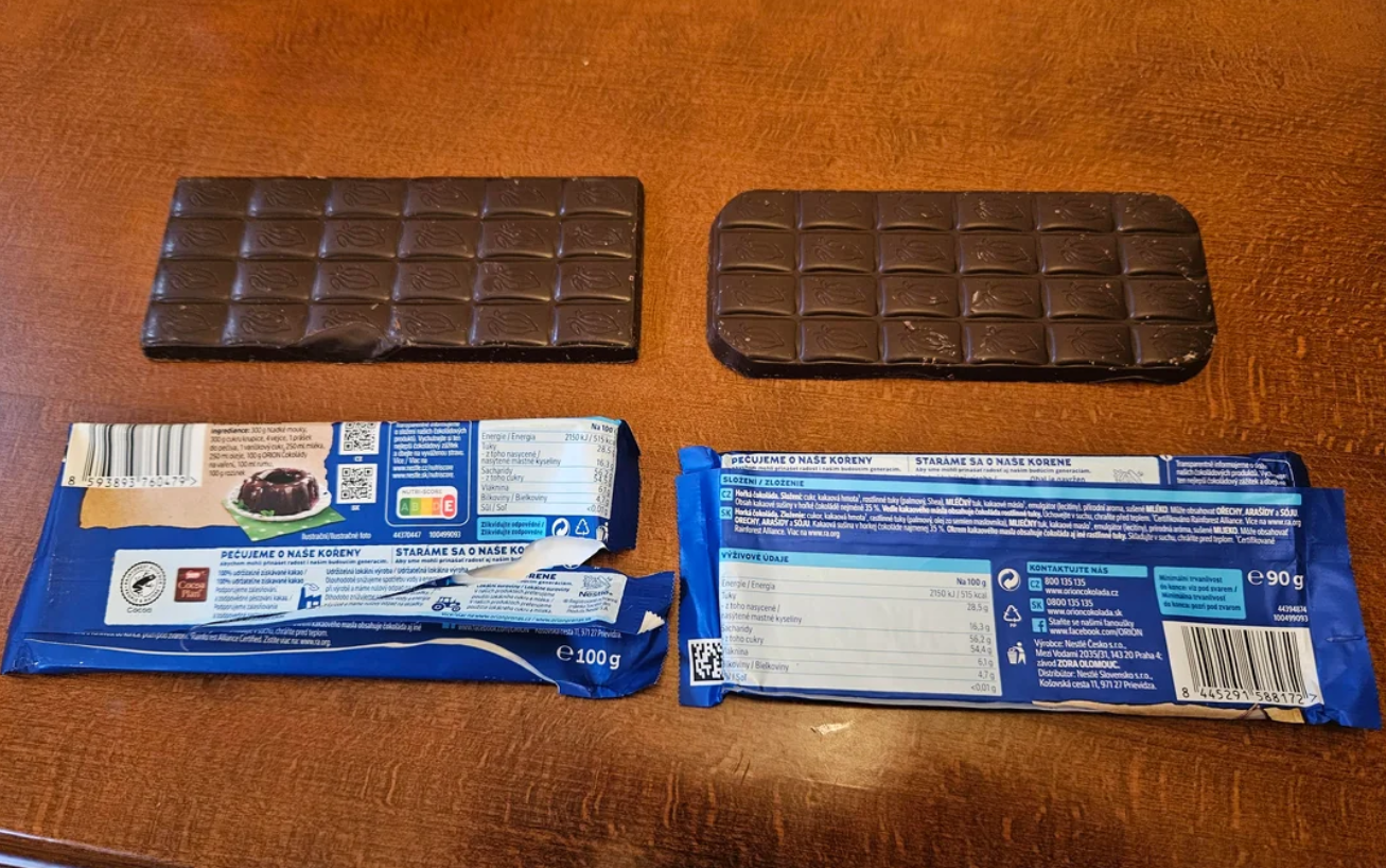 Two unwrapped dark chocolate bars lie side by side on a wooden surface, each above their respective blue wrappers, which are opened and show nutritional information and product details.