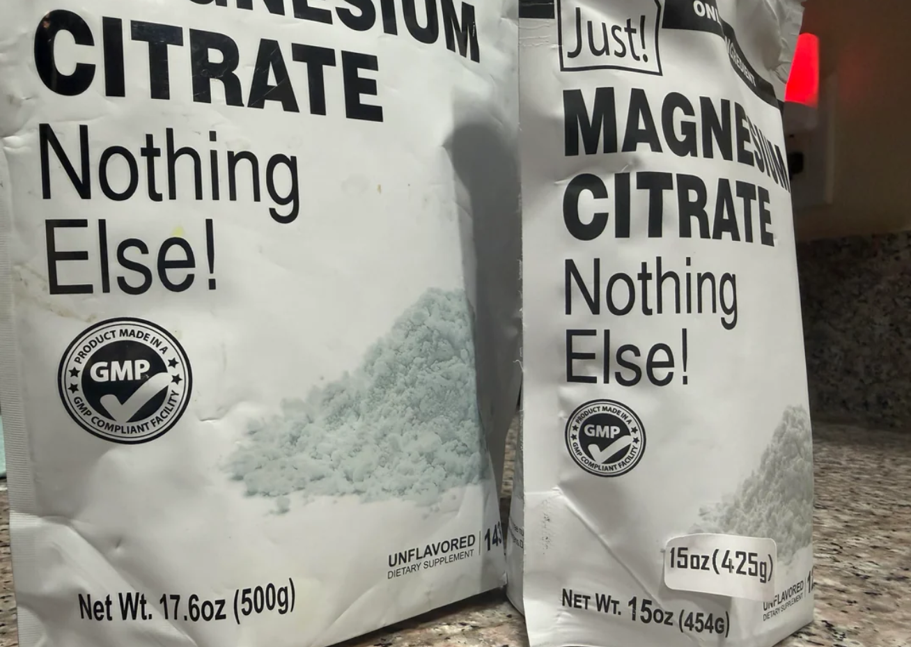 Two white bags of magnesium citrate powder on a granite countertop. The labels read “Nothing Else!” and display weights of 17.6 oz (500g) and 15 oz (425g and 454g), with GMP-certified seals visible.