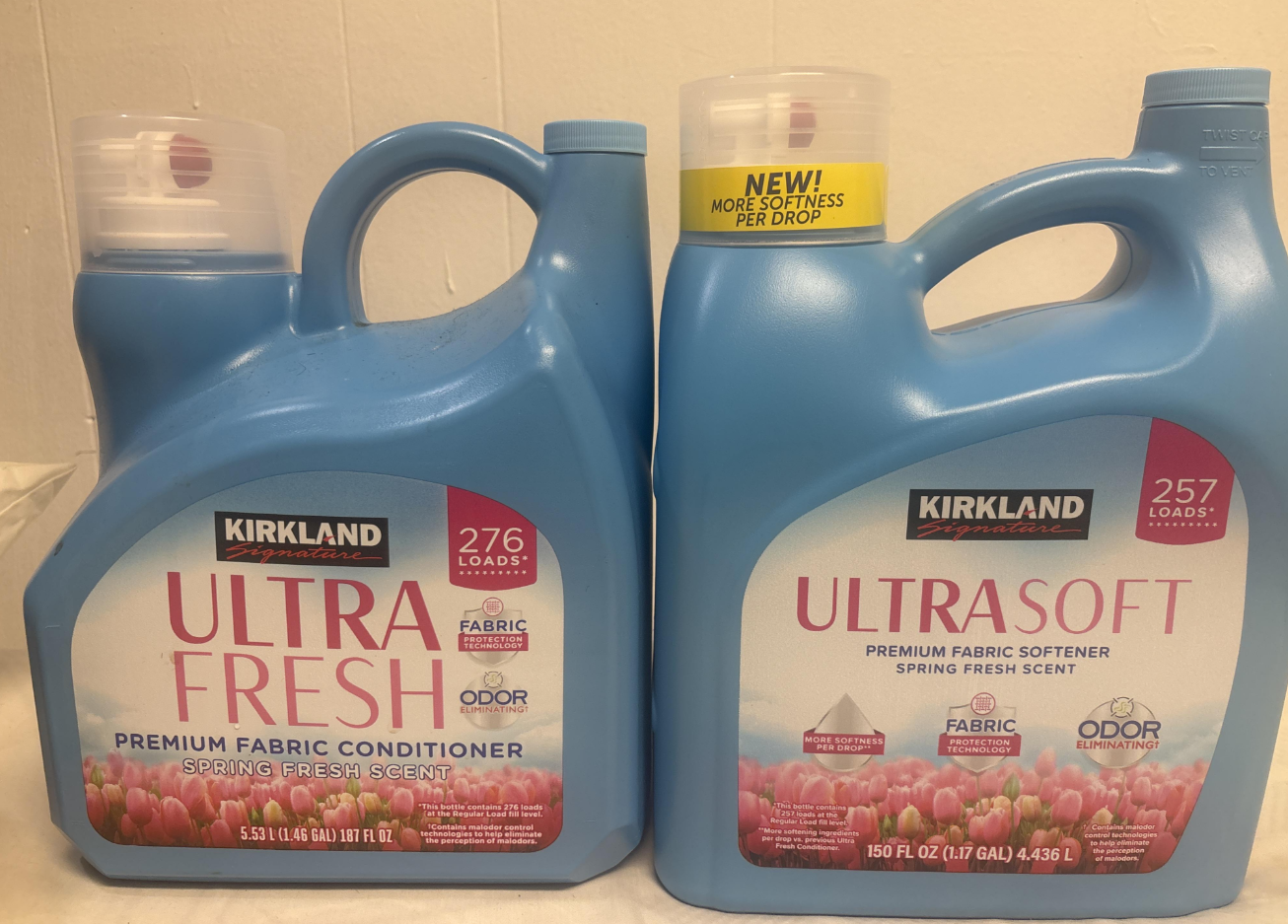 Two large blue containers of Kirkland brand fabric softener and conditioner, labeled "Ultra Fresh" and "Ultra Soft," stand side by side. Both feature pink lids and tulip images on their front labels.