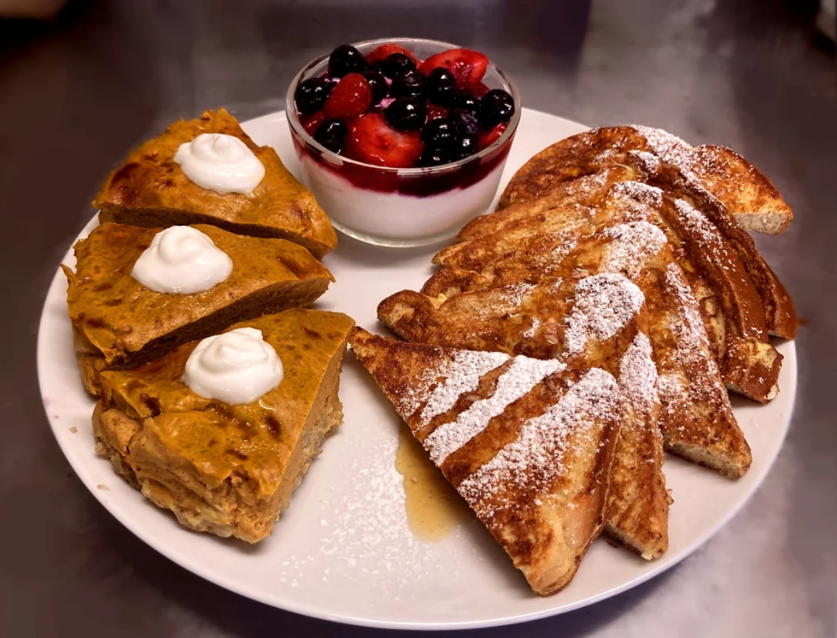 A plate with French toast topped with powdered sugar, pumpkin bread with dollops of cream, and a bowl of yogurt topped with mixed berries brings a sweet twist to classic dinners.