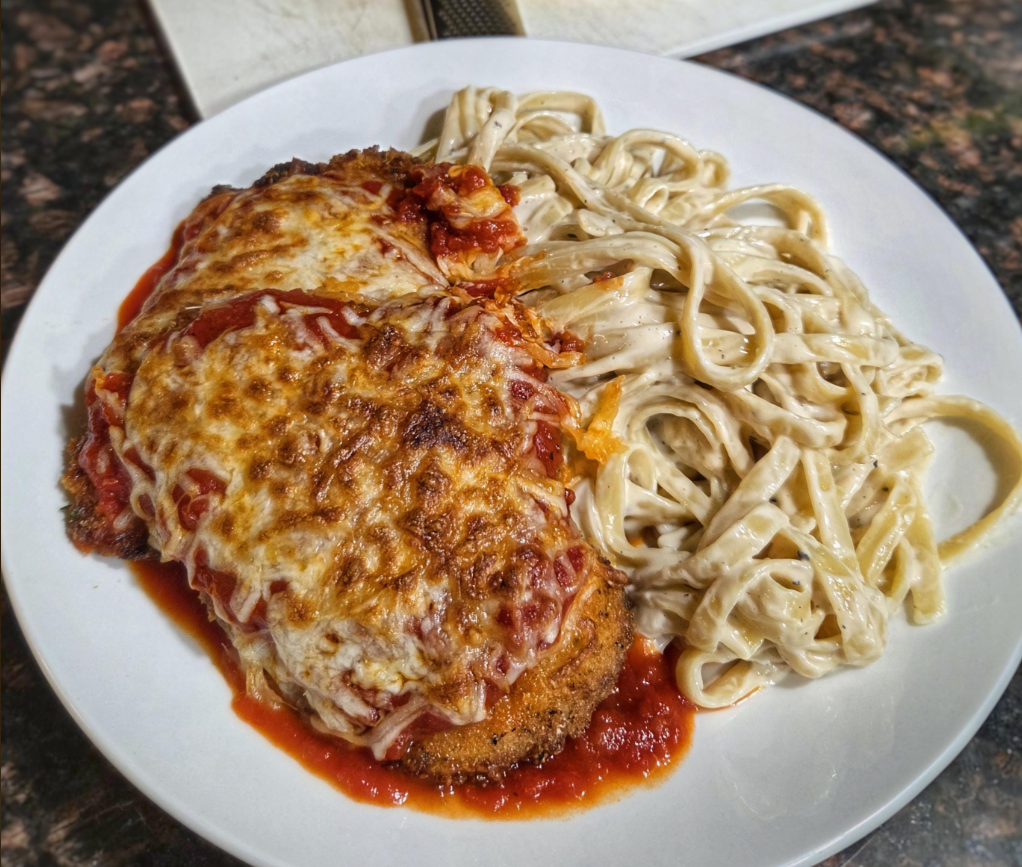 A plate of chicken parmesan topped with melted cheese and marinara sauce, served alongside creamy fettuccine Alfredo pasta on a white plate—an inviting choice for lovers of classic dinners.