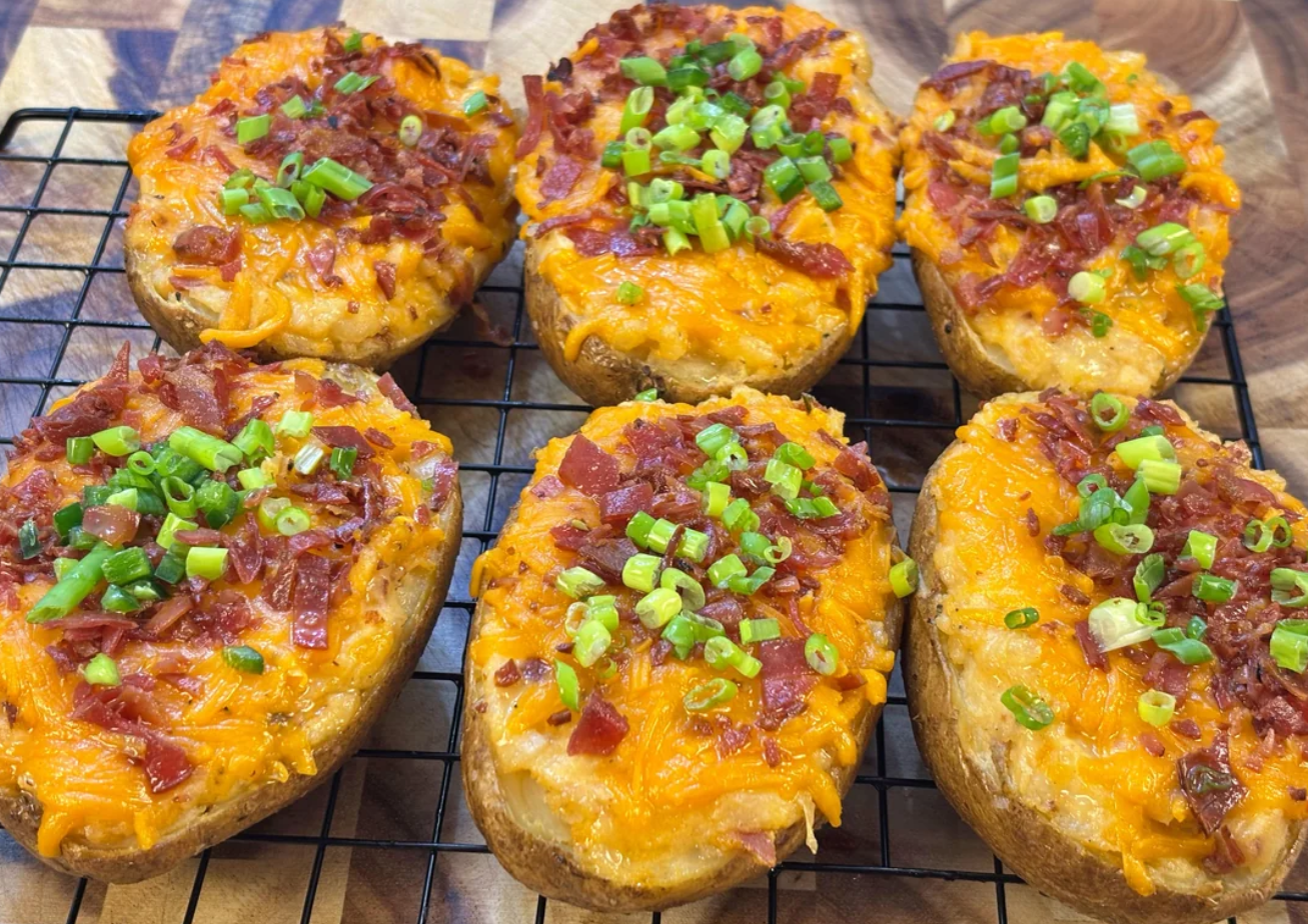 Six twice-baked potato halves topped with melted cheddar cheese, bacon pieces, and chopped green onions are cooling on a wire rack—a comforting favorite for busy middle class moms preparing family-friendly meals.