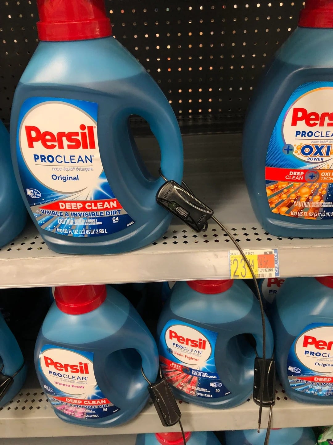 Large blue bottles of Persil ProClean laundry detergent, popular Walmart products, are displayed on a store shelf. One bottle has a security device on its handle, and a yellow sale tag showing $23 is visible below.