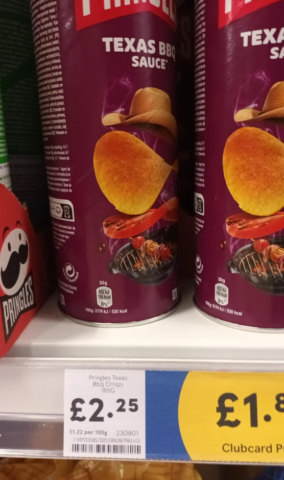 A can of Pringles Texas BBQ Sauce crisps is on a store shelf. The can features a crisp wearing a cowboy hat above a grill. The price label below reads £2.25 for 165g.