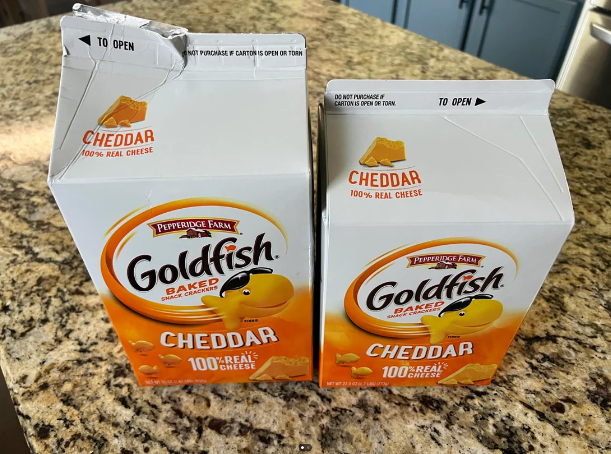 Two large boxes of Pepperidge Farm Goldfish Cheddar crackers sit on a granite countertop. Both open boxes reveal the brand logo, orange goldfish character, and cheddar cheese images—reminding you that sometimes you pay more for less.