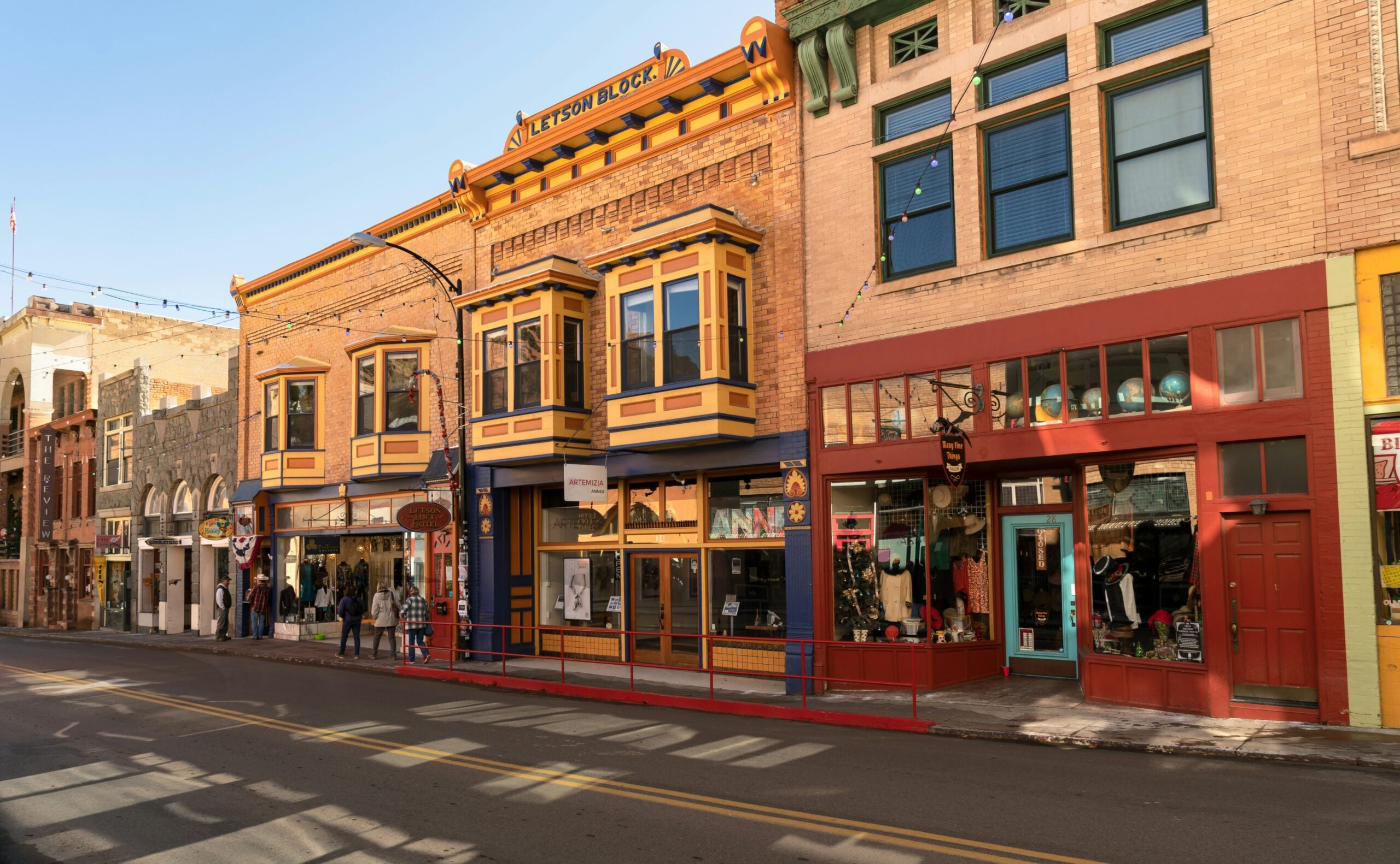 A row of colorful historic brick buildings with large windows and storefronts lines a sunny, empty street in one of the many unique American towns.
