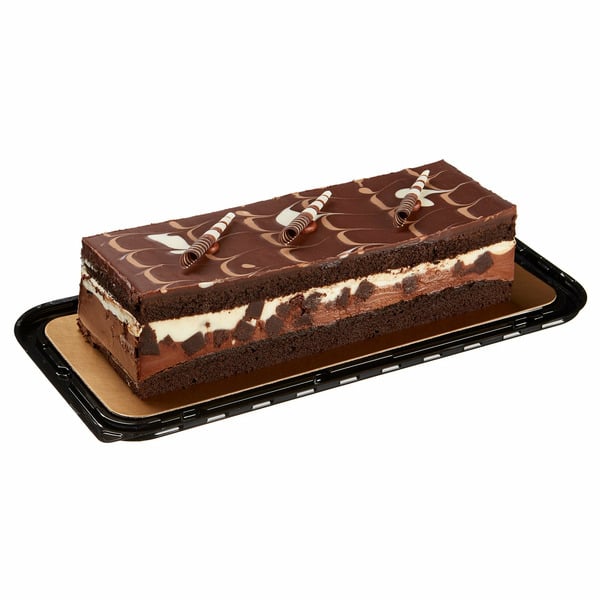 A rectangular chocolate layer cake with cream filling, chocolate decor on top, and three chocolate curls, displayed on a black plastic tray.