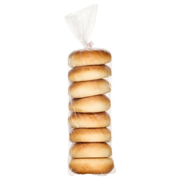 A clear plastic bag containing six plain bagels, stacked vertically, with the top of the bag twisted and sealed.