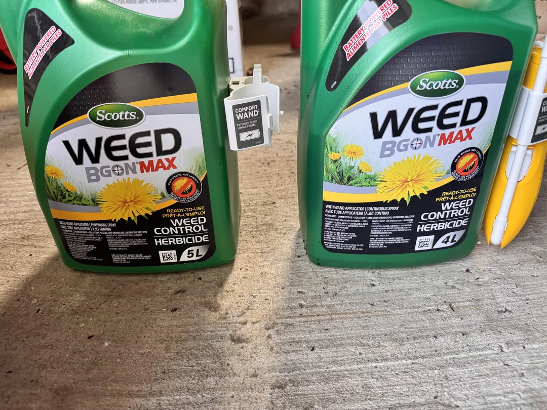 Two green containers of Scotts Weed B Gon Max weed control herbicide, one 5L and one 4L, are placed side by side on a concrete floor. A yellow and white comfort wand attachment is visible on the right.