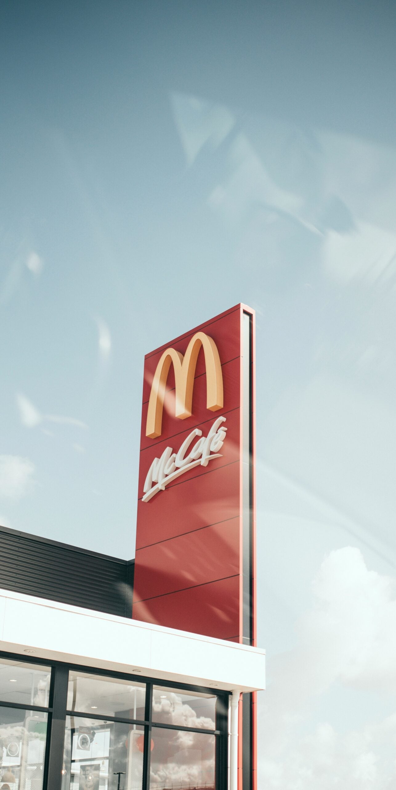 A tall red McDonald's sign with the yellow "M" logo and "McCafé" text stands outside a McDonald's restaurant under a clear blue sky.