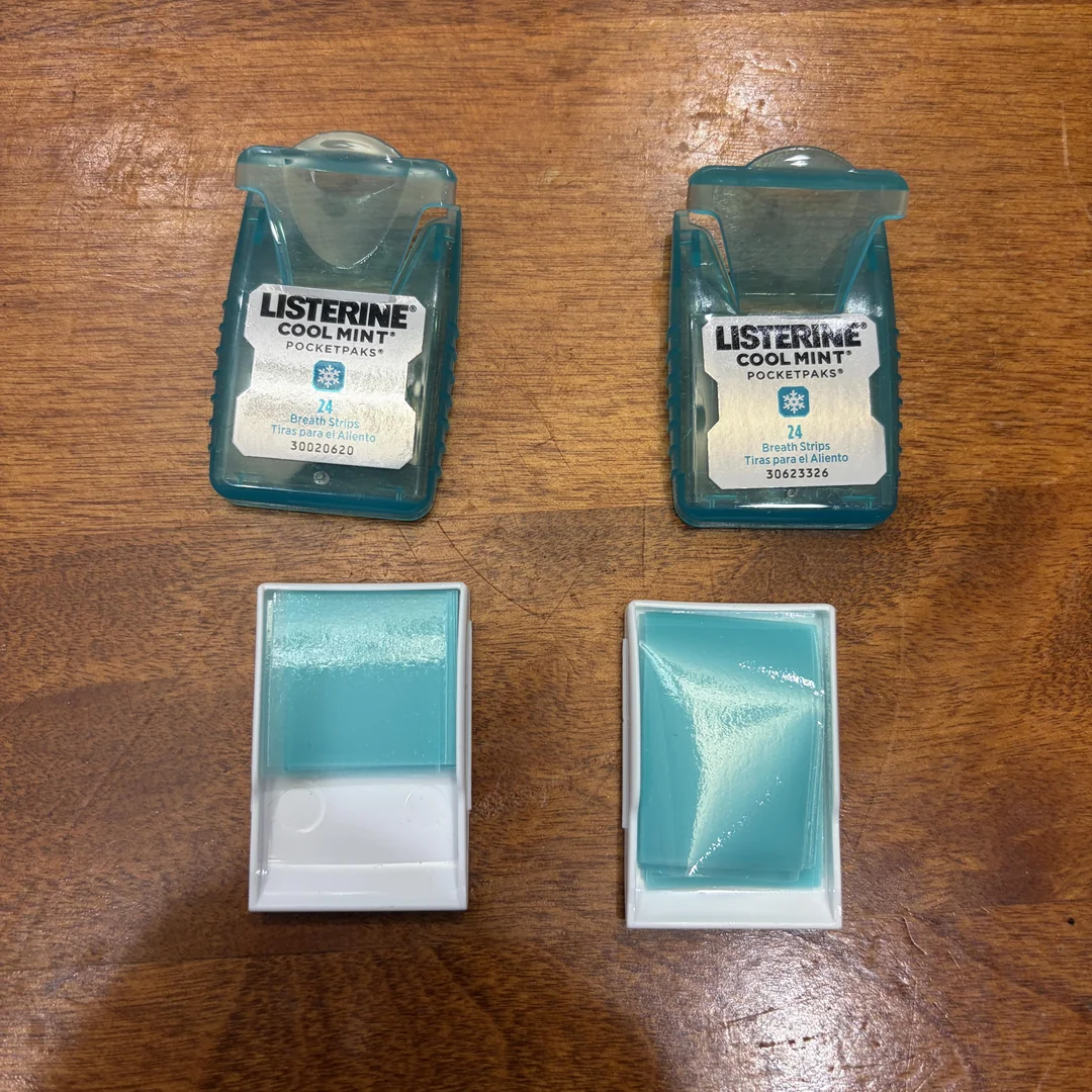 Two Listerine Cool Mint PocketPaks containers, often mentioned in shrinkflation products discussions, sit on a wooden surface with lids open and blue mint strips visible in white plastic trays.