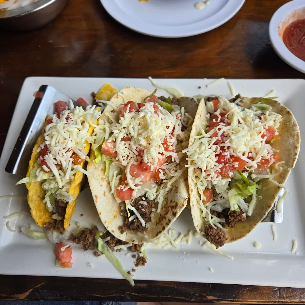 A rectangular plate with four tacos, each filled with ground beef, shredded lettuce, diced tomatoes, and grated cheese. One taco has a hard shell, while the others have soft flour tortillas.
