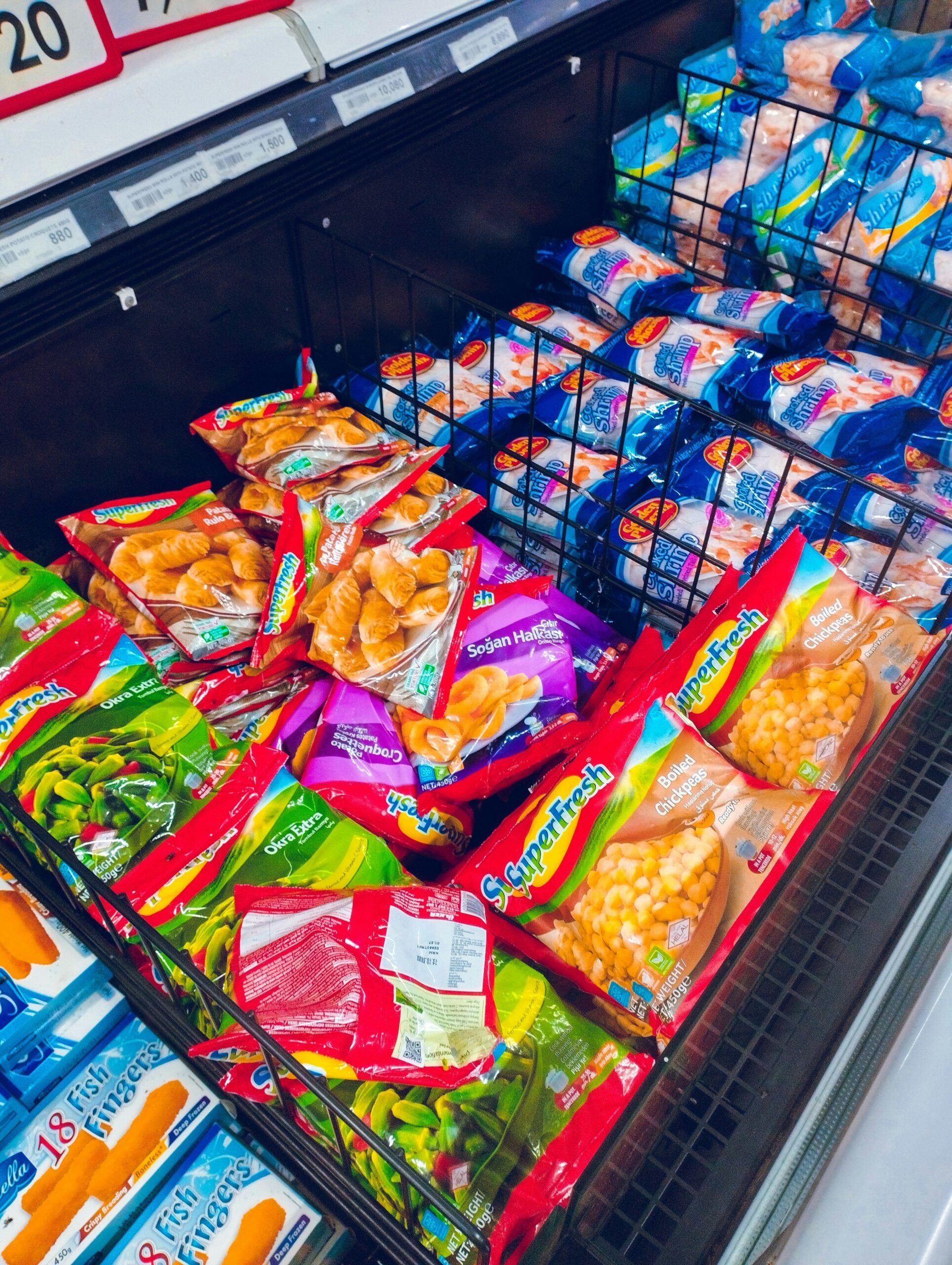 Bags of frozen vegetables and potato products from various brands are displayed in a grocery store freezer section. The packages include green beans, peas, and hash browns in colorful packaging.