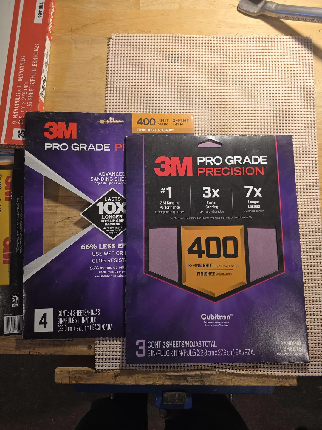 Two packages of 3M Pro Grade Precision sanding sheets are on a textured surface. The left pack is labeled "4" and the right pack is "400 grit X-Fine," advertising longer sanding sheet life and better performance.