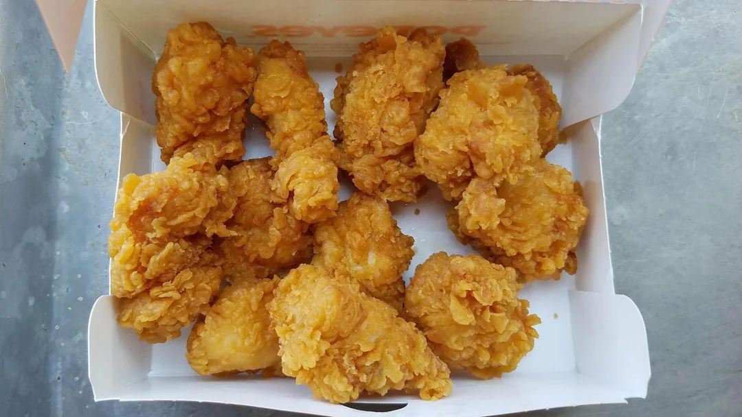 A white cardboard box filled with golden-brown, crispy fried chicken pieces placed on a gray surface.