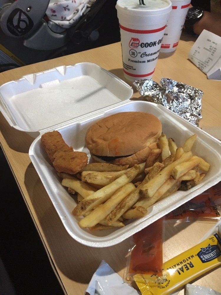 A styrofoam takeout container with french fries, a fried chicken strip, and a sandwich. A drink cup, foil wrapper, receipt, and condiment packets are on the table next to it.
