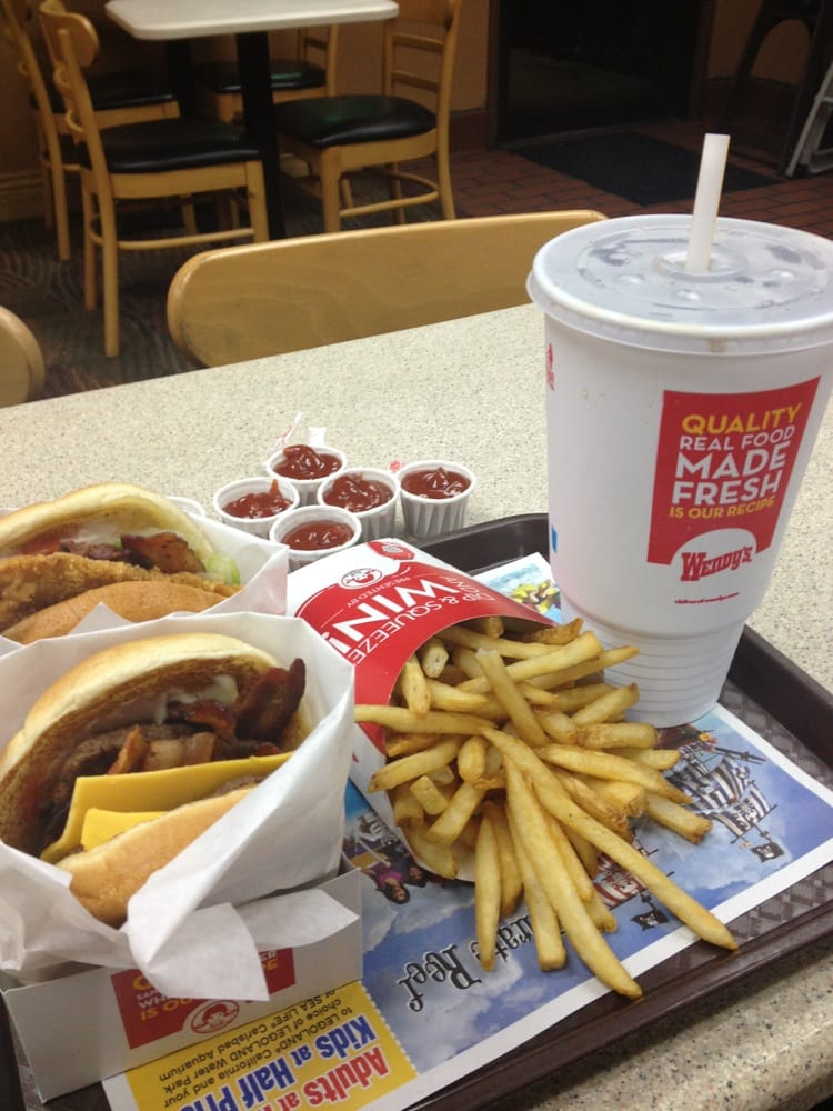 A fast food tray with a cheeseburger, a chicken sandwich, french fries, multiple ketchup cups, and a large Wendy’s soft drink cup highlights classic burger chain value on a table in the restaurant.