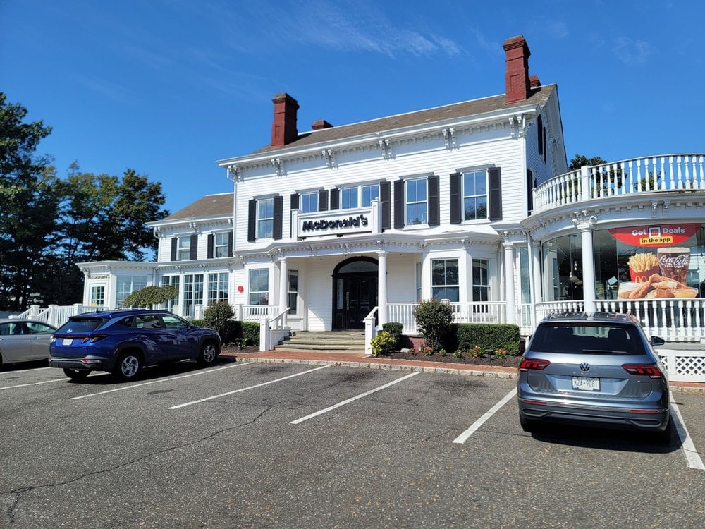 A McDonald's restaurant in a large, white, colonial-style building with tall windows, two chimneys, and a wraparound porch—one of the Coolest McDonald's Locations. Several cars are parked in front, and a McDonald's sign is above the entrance.
