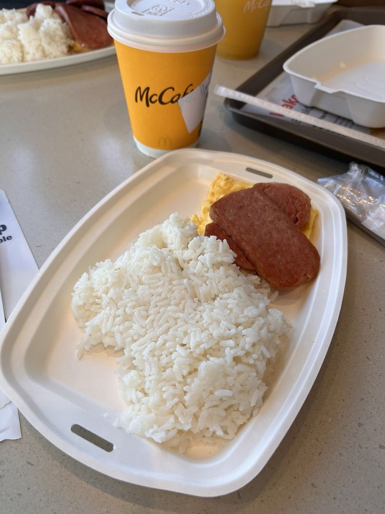 A breakfast meal at one of the Coolest McDonald's Locations features white rice, two slices of cooked luncheon meat, and scrambled eggs on a tray, served alongside a McCafé coffee cup.