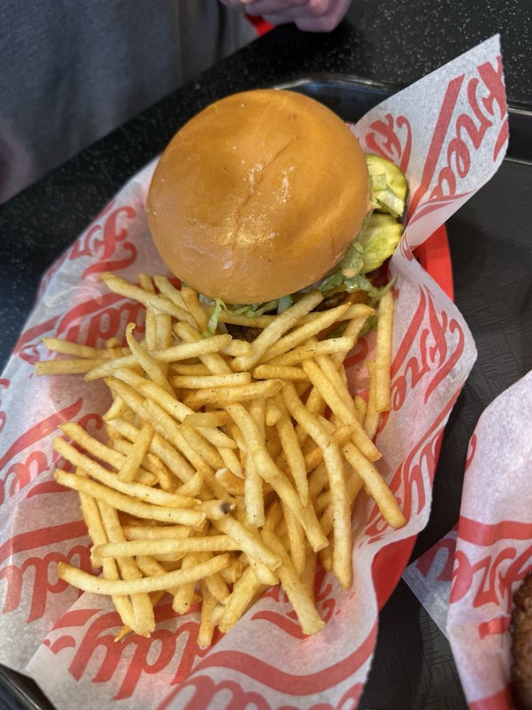 A tray with a burger in a soft bun and a generous serving of thin, crispy French fries, served on red and white branded paper.
