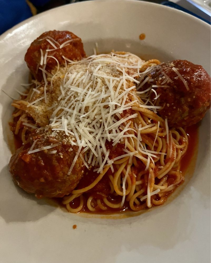 A white bowl filled with spaghetti topped with marinara sauce, four large meatballs, and a generous sprinkle of shredded parmesan cheese—just like you’d find at the Best Italian Restaurants.