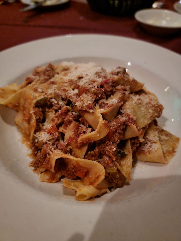 A white plate filled with pappardelle pasta topped with a hearty meat sauce and sprinkled with grated cheese, just like you'd find at the Best Italian Restaurants, set on a table with a blurred background.