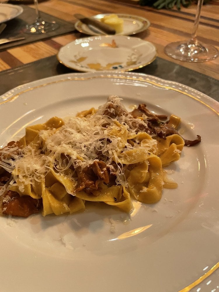 A plate of pasta topped with grated cheese and mushrooms sits on a table, set in the elegant ambiance typical of the Best Italian Restaurants, with a bread plate, butter knife, and wine glasses in the background.