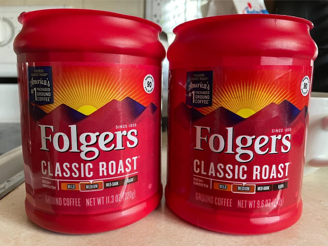 Two red containers of Folgers Classic Roast ground coffee, a staple among Coffee Brands, are placed side by side on a countertop. The sunrise graphic and labels highlight their different net weights.