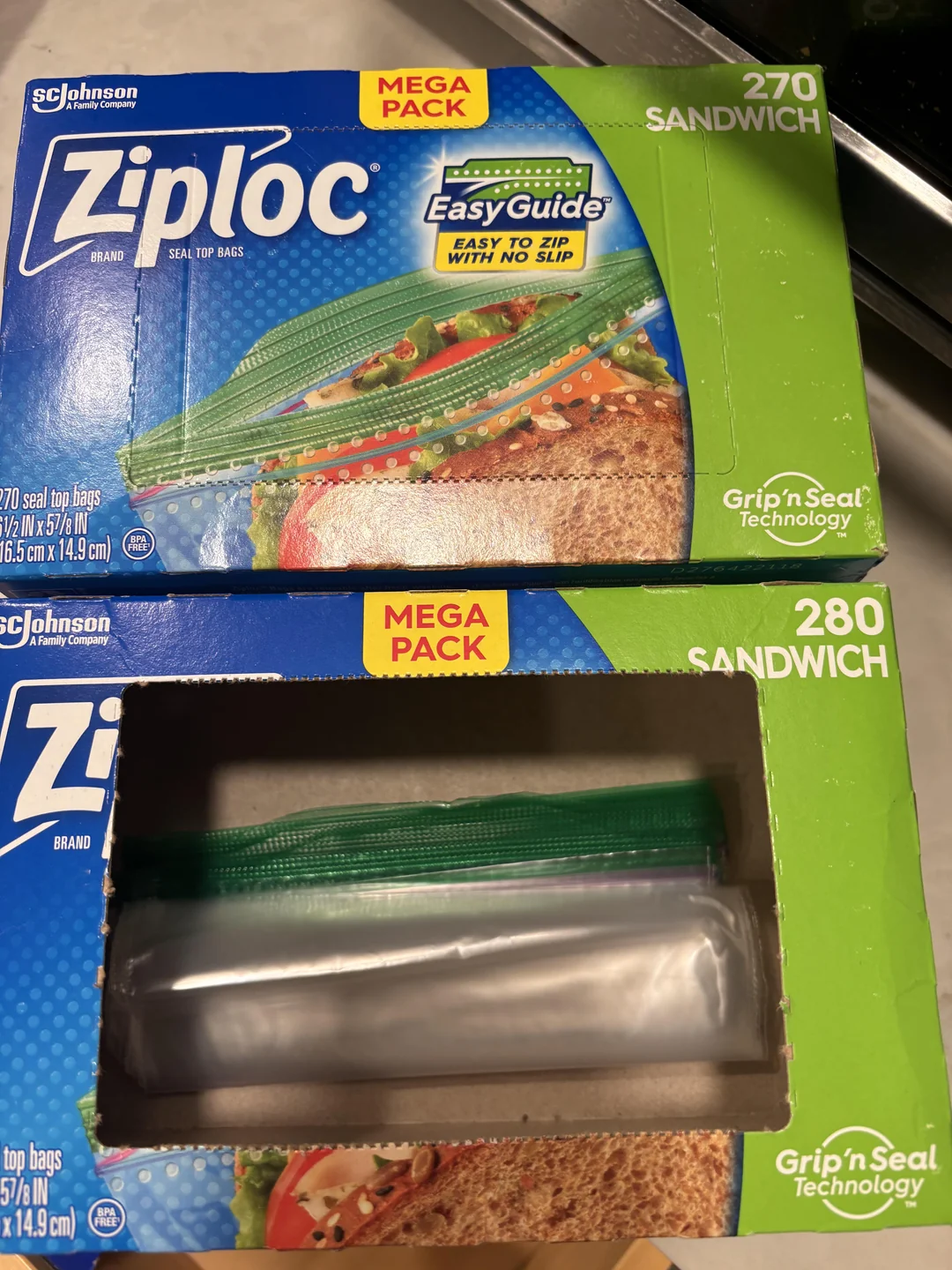 Two mega packs of Ziploc sandwich bags are shown. One unopened box displays the front label; the other box is open, revealing plastic bags inside. The boxes advertise Easy Guide and Grip 'n Seal technology.