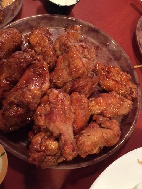A plate filled with crispy fried chicken wings coated in a shiny sauce, sitting on a wooden table with other dishes partially visible around it.