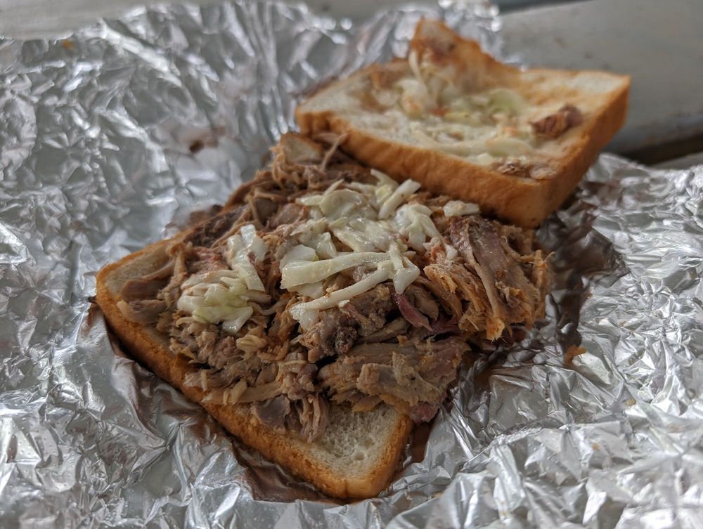 An open-faced pulled pork sandwich with chopped coleslaw on white bread, served on crinkled aluminum foil.
