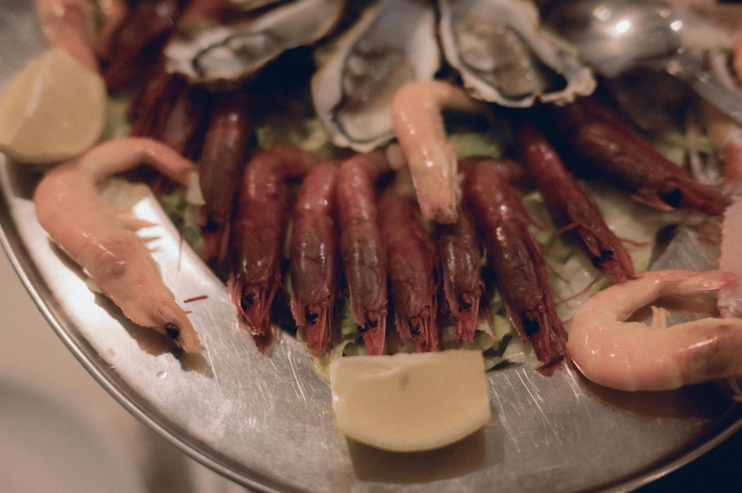 A metal platter with red and pink shrimp, oysters on the half shell, lemon wedges, and a bed of shredded lettuce.