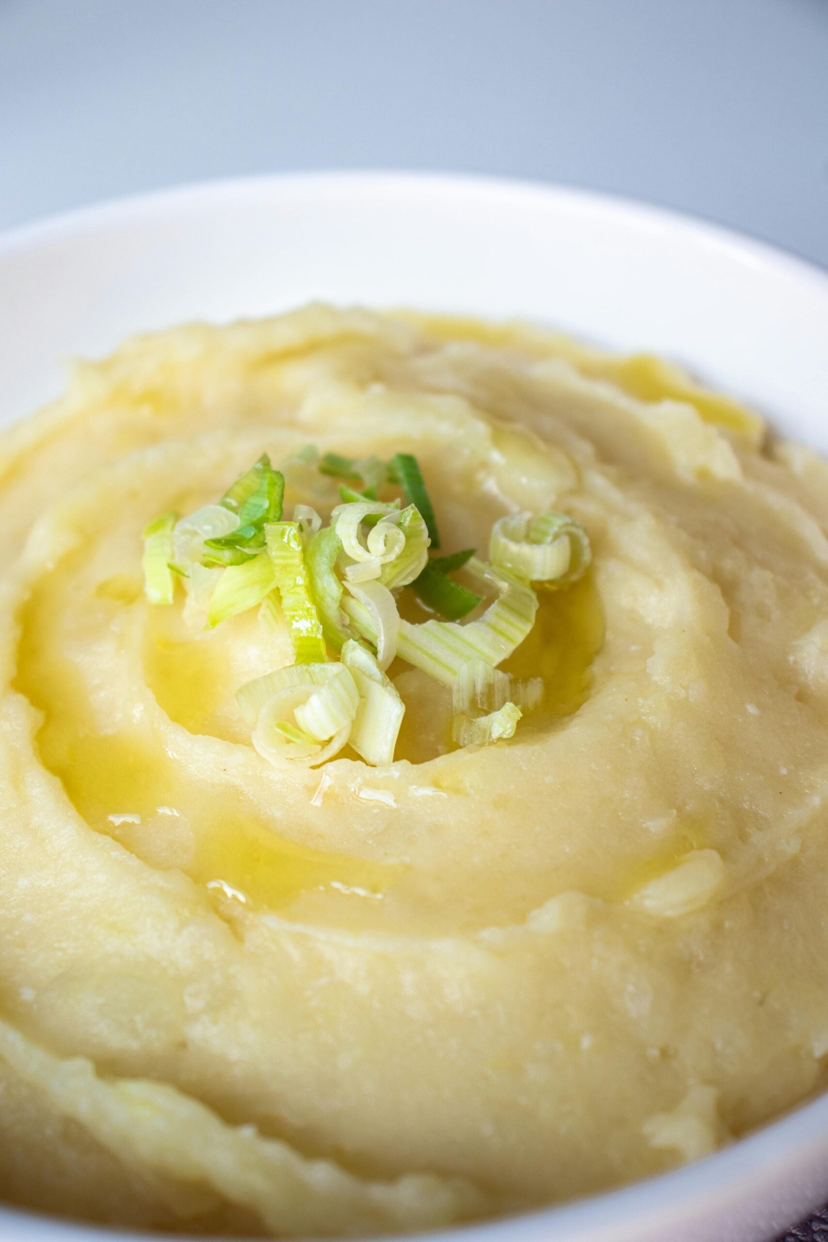 A white bowl filled with creamy mashed potatoes, topped with chopped green onions and a drizzle of melted butter.