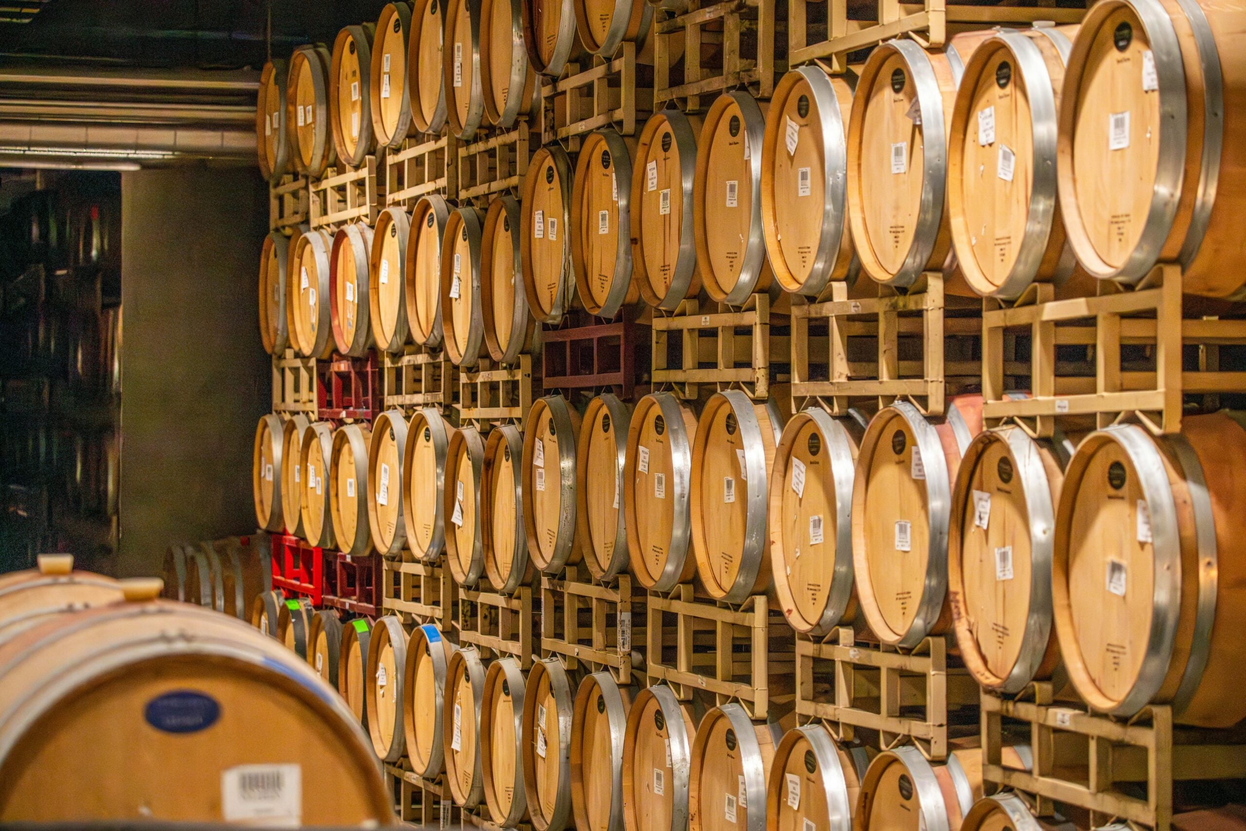 Rows of wooden wine barrels stacked on racks inside a cellar, creating a warm, organized pattern along the walls.