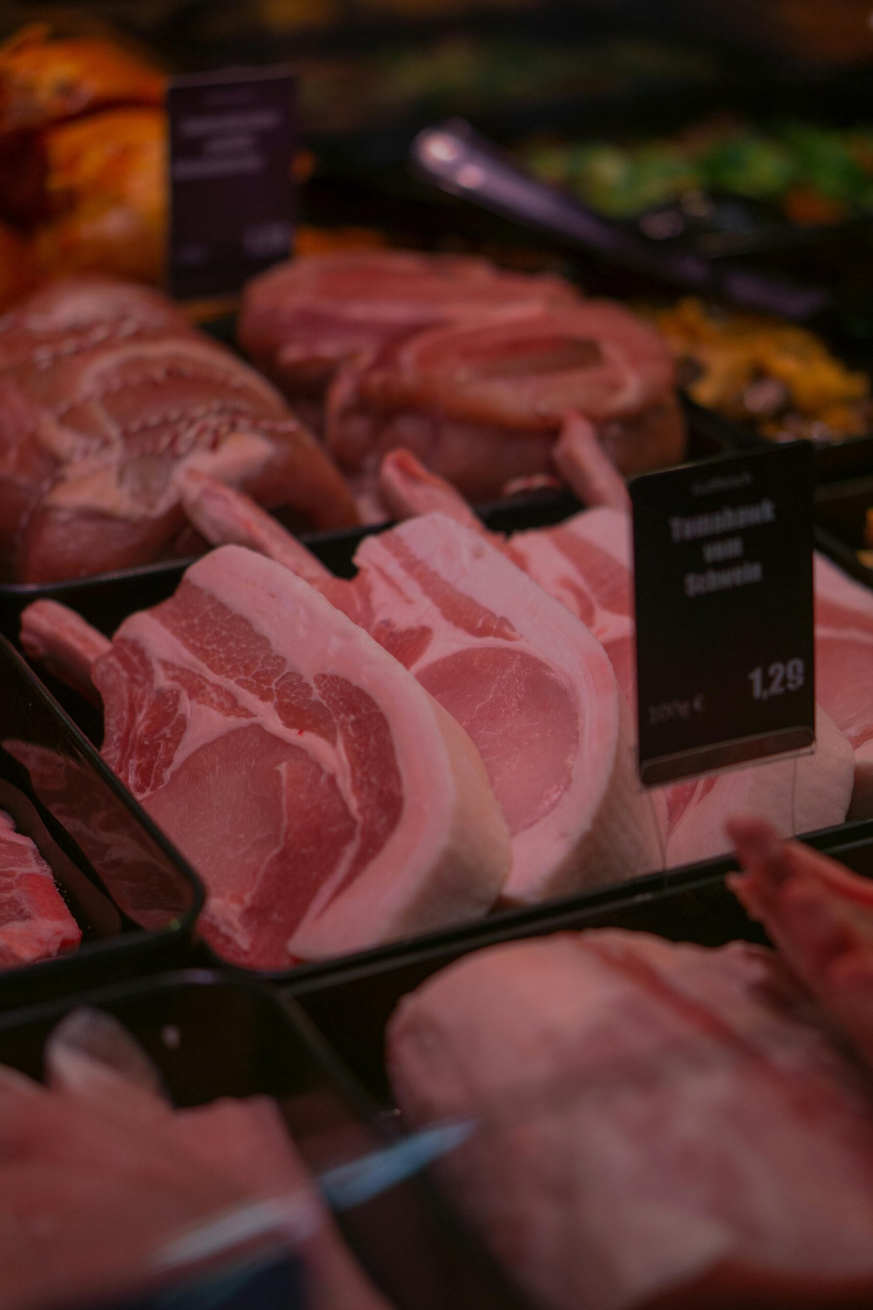 Raw pork chops and other cuts of meat displayed in a market or butcher's counter, with price labels visible. The meat is arranged in black trays.