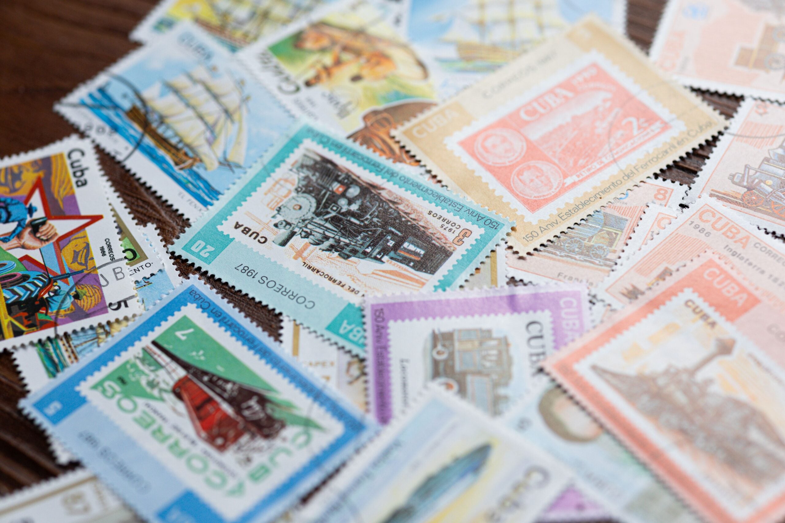A scattered collection of colorful Cuban postage stamps featuring various designs, including ships, trains, and historical illustrations, spread out on a wooden surface.