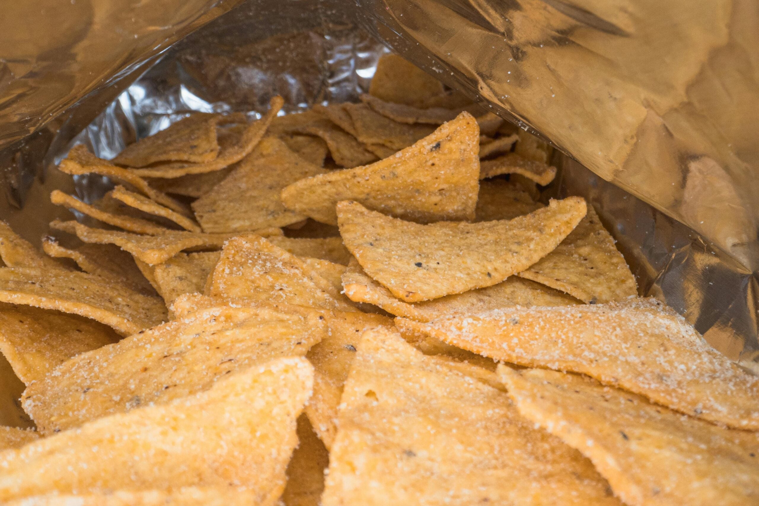 Close-up view inside an open bag of tortilla chips, showing several seasoned, triangular chips with a light dusting of salt and spices.