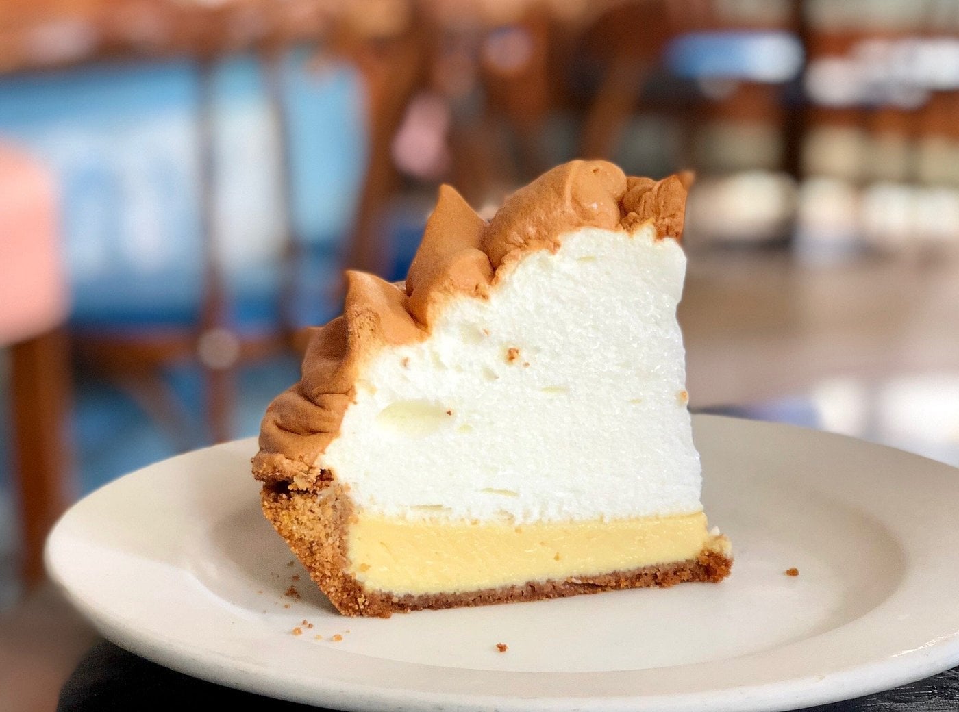 A slice of lemon meringue pie sits on a white plate, featuring a golden-brown crust, a yellow lemon filling, and a tall layer of fluffy, lightly browned meringue—an irresistible choice at classic road trip food stops.