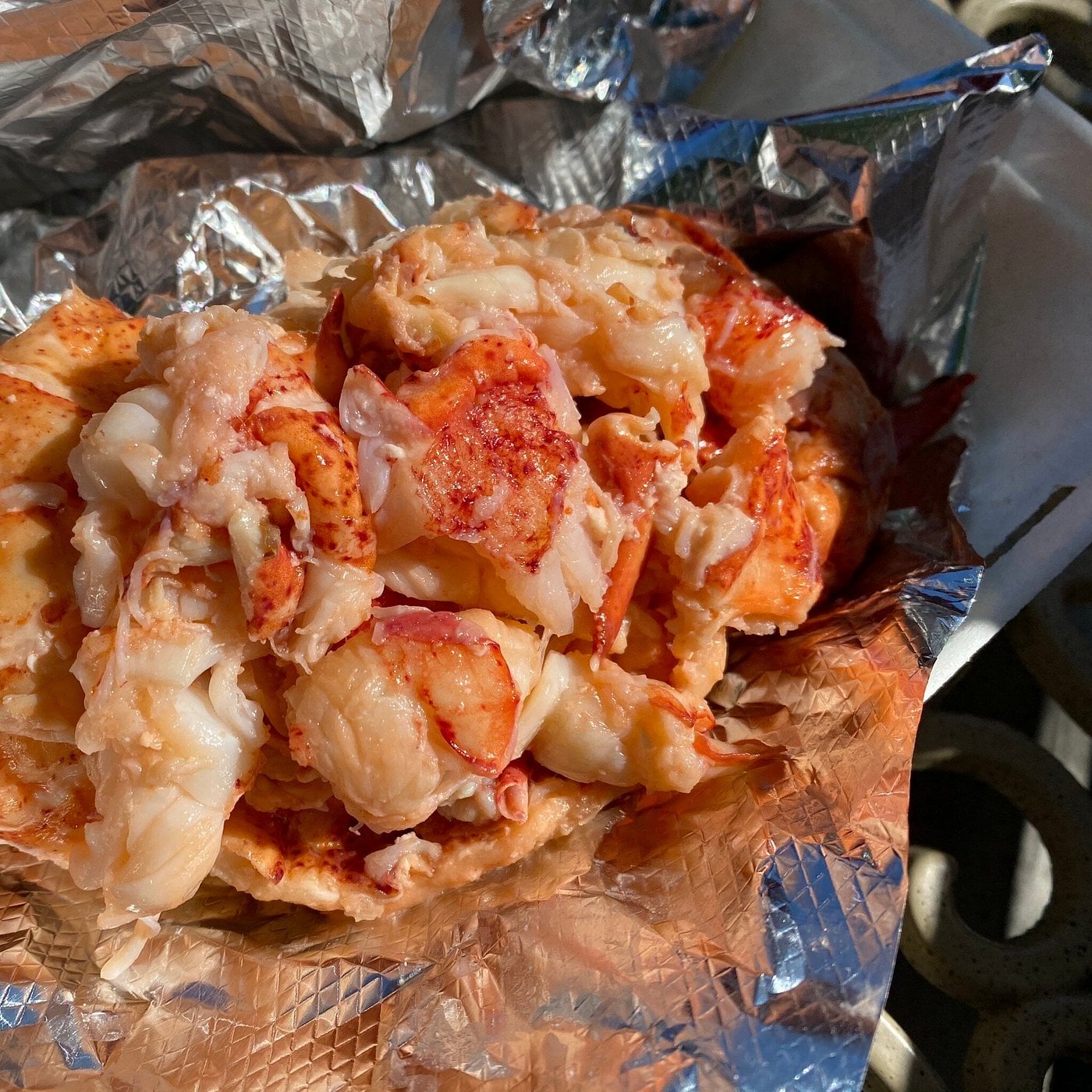 Chunks of lobster meat sit on crinkled aluminum foil, glistening in the sunlight—a perfect find for road trip food stops—with pieces of claw and tail in a rich, buttery sauce.