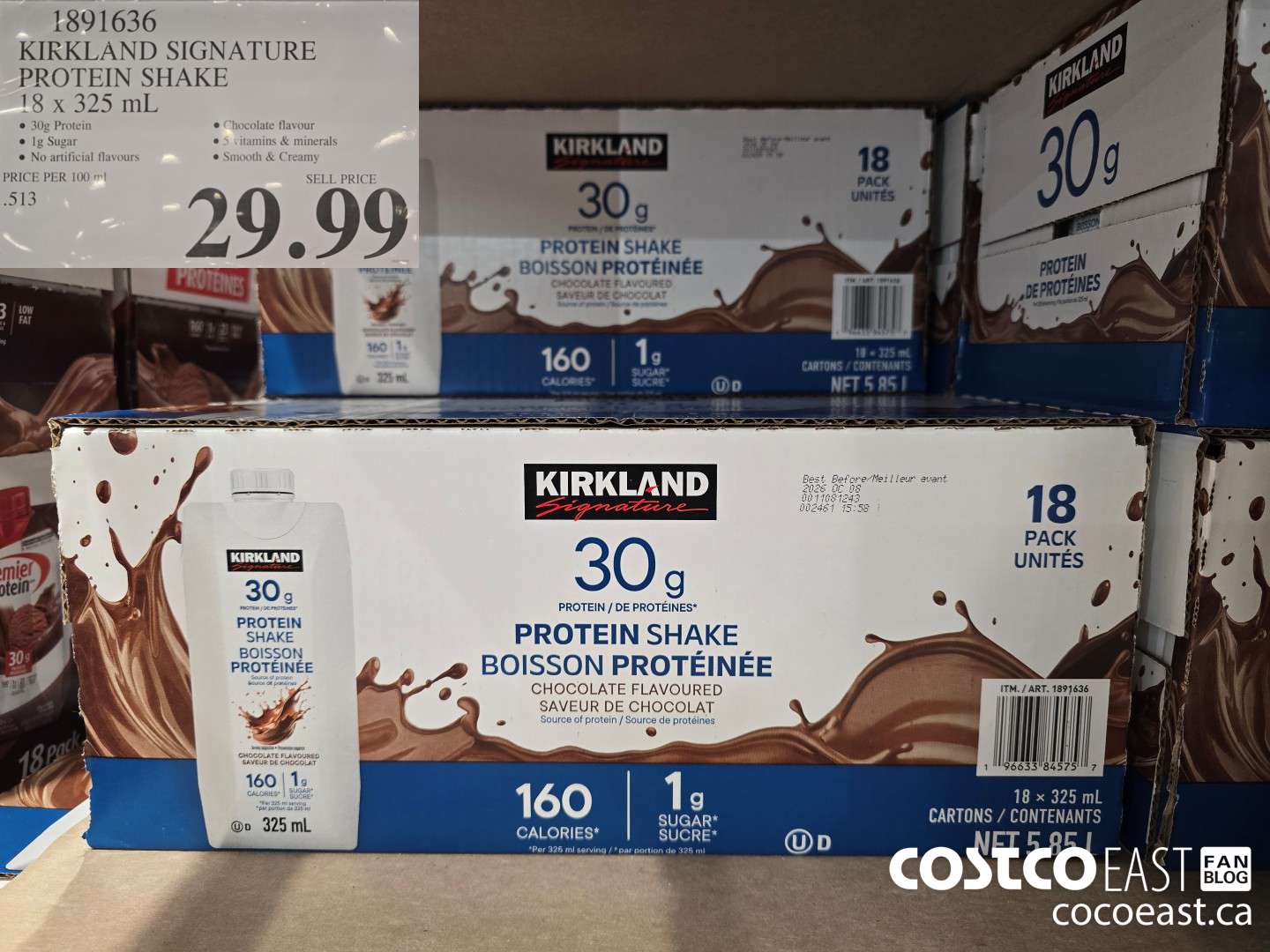 Boxes of Kirkland Signature Protein Shake, chocolate flavor, displayed on a store shelf. Each pack contains 18 bottles of 325 mL, with 30g protein, 1g sugar, and 160 calories per serving. Price tag shows $29.99.