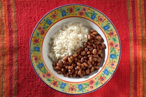 A colorful, floral-patterned bowl filled with rice and beans sits on a vibrant red woven tablecloth, creating a cheerful and inviting scene.