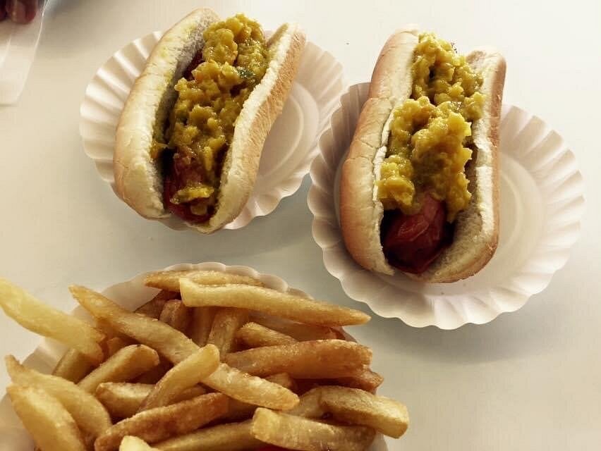 Two hot dogs topped with chopped relish sit in paper trays next to a serving of golden French fries—a classic choice at road trip food stops on a white surface.