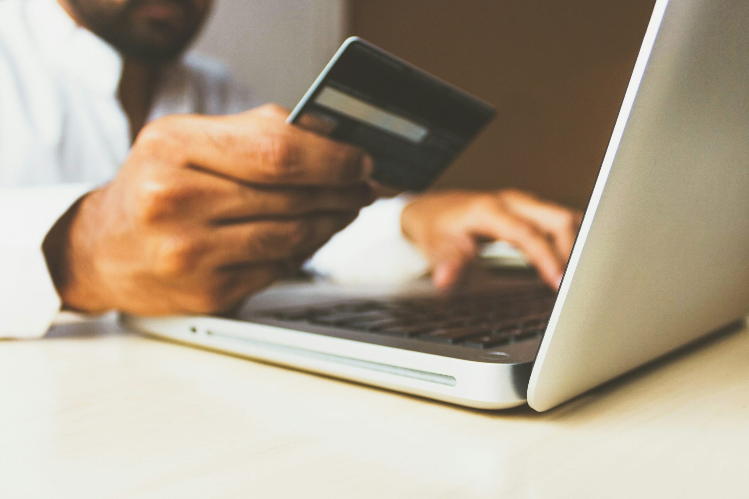 A person holding a credit card in one hand and typing on a laptop with the other, suggesting online shopping or electronic payment.
