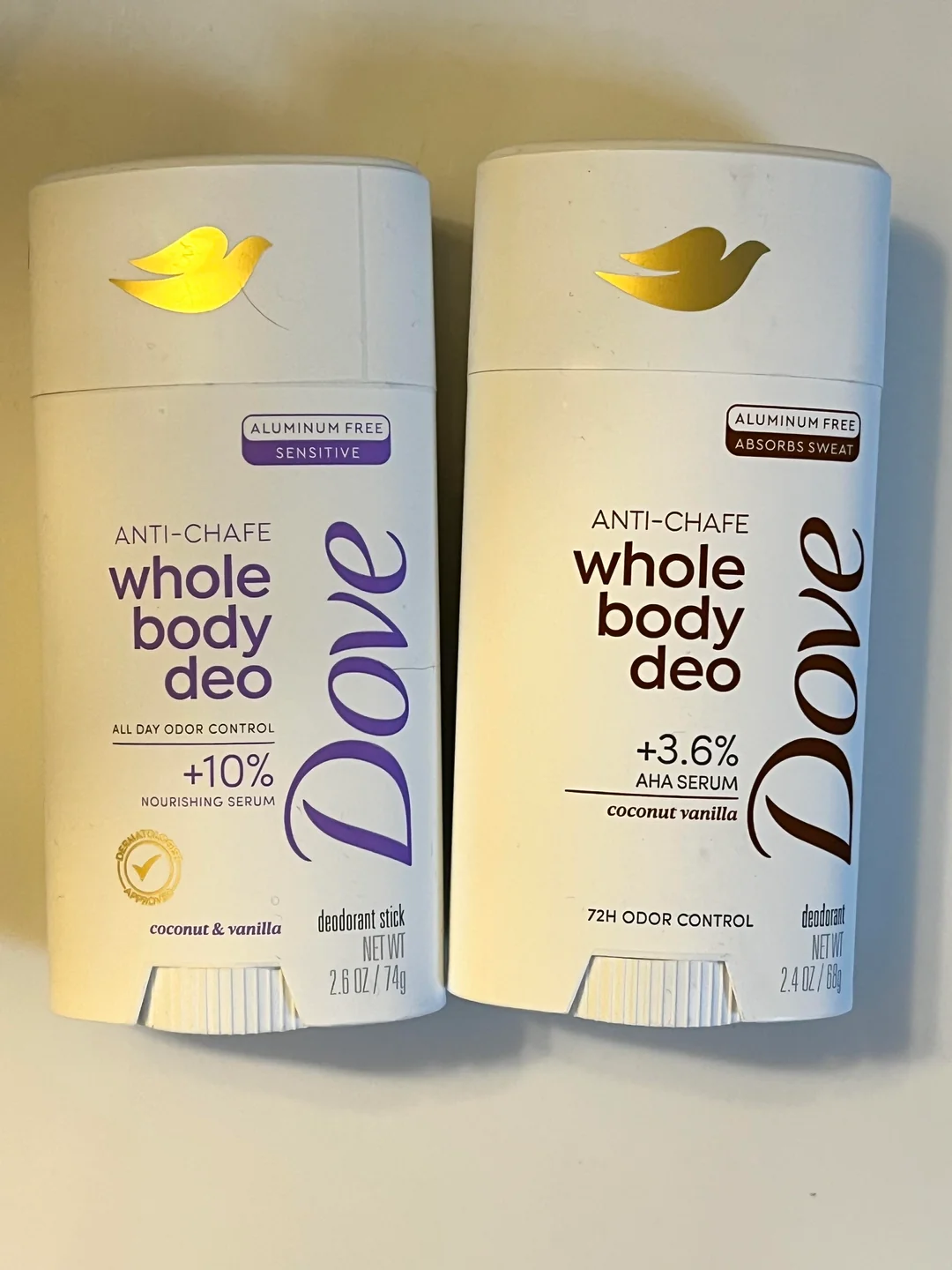 Two white Dove deodorant sticks are shown side by side. Both are labeled "whole body deo" in coconut & vanilla scent, with gold dove logos, and details about being aluminum free and providing odor control.