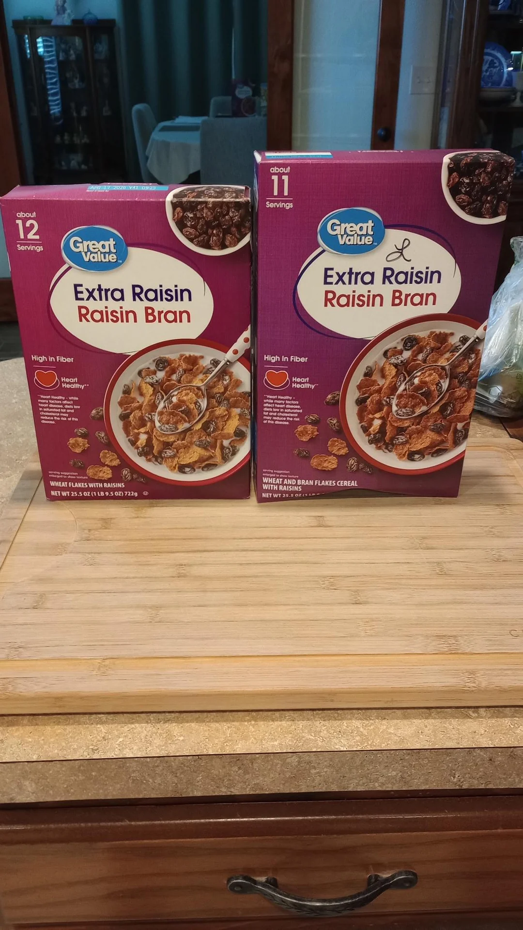 Two boxes of Great Value Extra Raisin Raisin Bran cereal are on a wooden cutting board. One box has 12 servings, the other has 11 servings. Both boxes feature images of the cereal in a bowl with milk.
